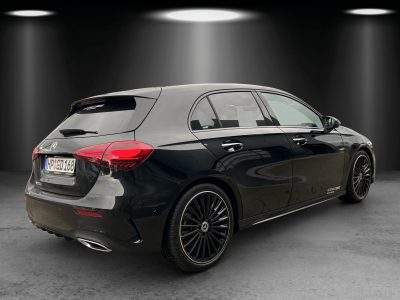 Heck- und Seitenansicht eines schwarzen Mercedes-Benz Kompaktwagens in einem Studio-Setup mit Spotbeleuchtung. Ausgestattet mit AMG-Line Exterieur, getönten Scheiben, zweiflutiger Endrohranlage und schwarzen mehrspeichigen Leichtmetallrädern.