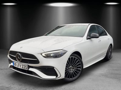 Frontansicht einer weißen Mercedes-Benz Limousine mit sportlichem AMG-Styling-Paket. Zu sehen sind der markante Diamantgrill mit zentralem Mercedes-Stern, LED-Scheinwerfer, große Lufteinlässe sowie schwarze Leichtmetallräder im Mehrspeichen-Design. Fahrzeug steht in einem Studio mit neutraler Ausleuchtung und dunklem Hintergrund.