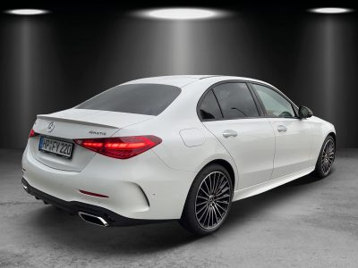 Rückansicht einer weißen Mercedes-Benz Limousine mit 4MATIC-Allradantrieb. Fahrzeug steht in einem Studio mit dunklem Hintergrund und Spotlights. Elegantes Design mit LED-Rückleuchten, sportlichem Diffusor und zweiflutiger Abgasanlage. Schwarz polierte Mehrspeichen-Leichtmetallräder unterstreichen den Premium-Charakter.