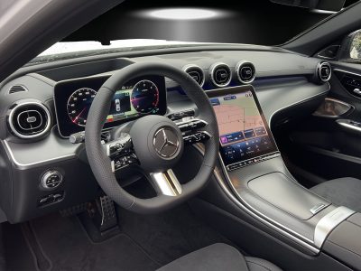Innenraum eines Mercedes-Benz mit modernem Cockpit – Multifunktionslenkrad mit Mercedes-Stern, digitales Kombiinstrument mit Tachometer und Navigation, zentraler Touchscreen mit Navigationsanzeige, stilvolle Luftdüsen im Turbinen-Design, Ambiente-Beleuchtung in Blau, sportlich-elegante Mittelkonsole in Carbon-Optik.