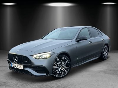 Front- und Seitenansicht eines mattsilbernen Mercedes-AMG mit LED-Scheinwerfern, Panamericana-Kühlergrill, sportlicher Frontschürze und markanten AMG-Leichtmetallrädern – fotografiert in einem Studio-Setup mit gerichteter Beleuchtung.