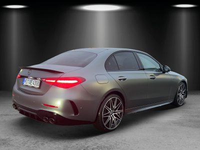 Heckansicht eines mattsilbernen Mercedes-AMG mit LED-Rückleuchten, Sportauspuffanlage mit vier Endrohren, schwarzem Diffusor und AMG-Leichtmetallrädern – fotografiert in Studioatmosphäre mit Spotbeleuchtung.