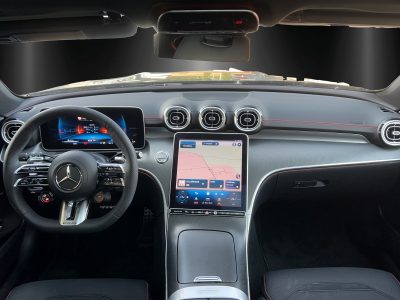 Cockpit eines Mercedes-Benz mit digitalem Kombiinstrument hinter dem Lenkrad und großem Touchscreen in der Mittelkonsole. Runde Lüftungsdüsen und rote Ziernähte auf dem Armaturenbrett.