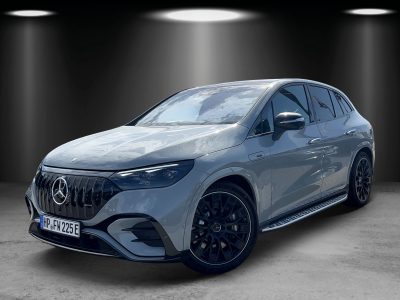 Front-/Seitenansicht eines grauen Mercedes-AMG EQE 43 SUV mit typischem AMG-Panamericana-Kühlergrill, sportlichen schwarzen Felgen und seitlichem EQE-Emblem. Das Fahrzeug steht in einem Ausstellungsraum mit dunklem Hintergrund und Spotlicht-Inszenierung.