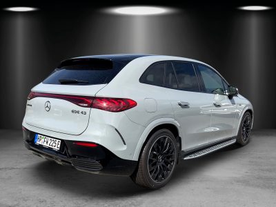 Heckansicht eines weißen Mercedes-AMG EQE 43 SUV mit schwarzem Dach, durchgehendem LED-Rücklicht, AMG-Schriftzug und stylischen schwarzen Felgen. Das Fahrzeug steht in einem Ausstellungsraum mit dunklem Hintergrund und Spotbeleuchtung.