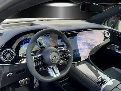 Innenraum eines Mercedes-AMG mit Hyperscreen-Display: Großflächiges digitales Cockpit, Sportlenkrad mit AMG-Emblem, Carbon-Zierelemente, Ambientebeleuchtung mit roter Naht auf dem Armaturenbrett, moderne Luftauslässe im Turbinen-Design.