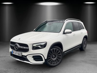 Front- und Seitenansicht eines weißen Mercedes-Benz SUV im Studio mit Spot-Beleuchtung – markanter Kühlergrill mit großem Stern, LED-Tagfahrlicht, schwarze Leichtmetallfelgen und Regen auf der Karosserie sichtbar.