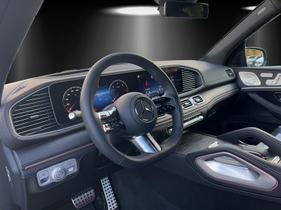 Innenraum eines Mercedes-AMG mit Blick auf das schwarze Multifunktionslenkrad, volldigitales Cockpit, Navigationsdisplay, Aluminium-Akzente, Ambientebeleuchtung und sportliches Armaturenbrett mit roten Kontrastnähten – modern und hochwertig gestaltet.