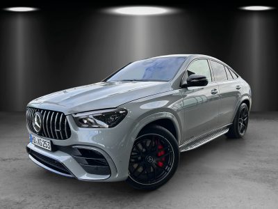 ercedes-Benz GLE 63 S AMG Coupé in hellgrauer Lackierung, fotografiert in einem Studio mit Spotbeleuchtung, Front- und Seitenansicht mit Panamericana-Kühlergrill, großen Lufteinlässen, roten AMG-Bremssätteln und schwarzen Leichtmetallrädern.