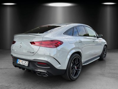 Mercedes-Benz GLE 63 S AMG Coupé in hellgrauer Lackierung, fotografiert in einem Studio mit Spotbeleuchtung, Heck- und Seitenansicht mit sportlichem Diffusor, vierflutiger Auspuffanlage und AMG-Leichtmetallrädern.
